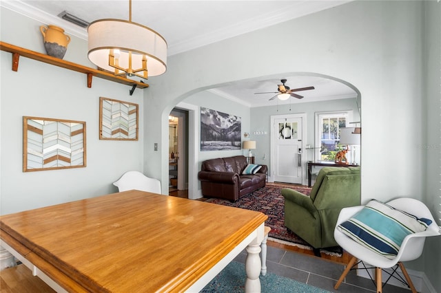 dining space with dark tile patterned floors, crown molding, and ceiling fan with notable chandelier