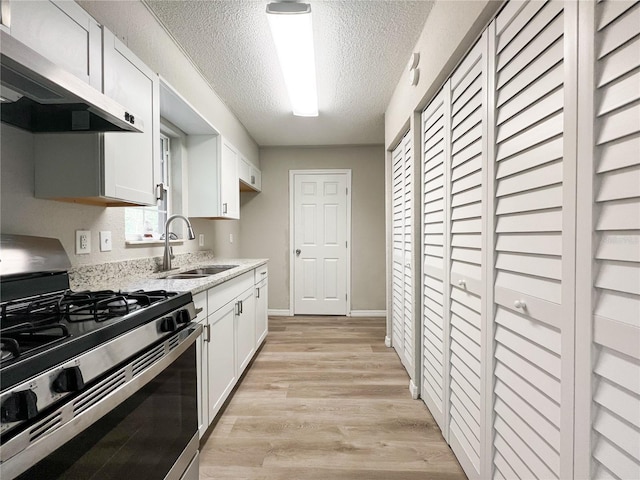 kitchen featuring stainless steel gas range oven, extractor fan, a textured ceiling, white cabinetry, and sink