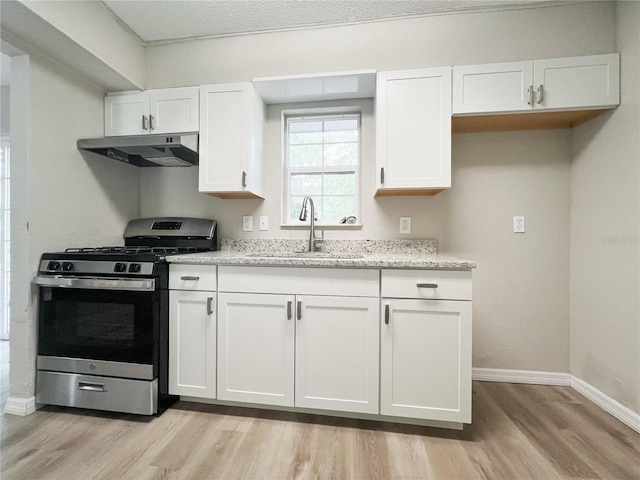 kitchen featuring stainless steel gas range, light wood-type flooring, light stone counters, sink, and white cabinetry