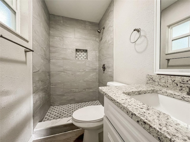 bathroom featuring toilet, a tile shower, and vanity