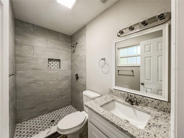 bathroom with toilet, tiled shower, and vanity