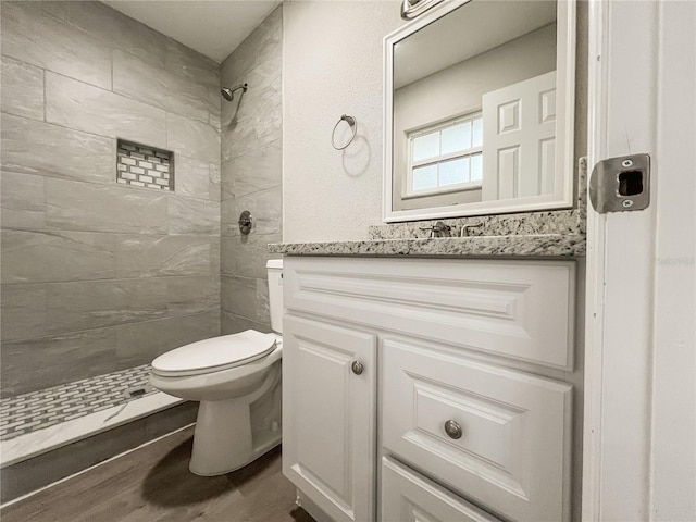 bathroom featuring toilet, hardwood / wood-style flooring, a tile shower, and vanity