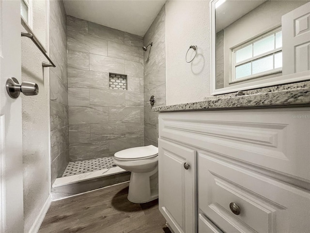 bathroom featuring tiled shower, toilet, vanity, and wood-type flooring