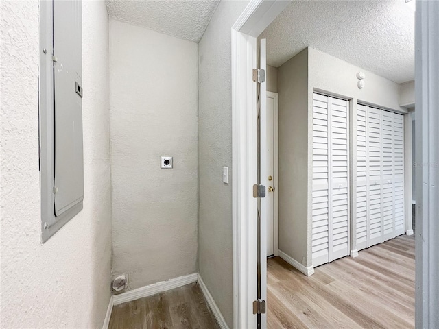 corridor featuring a textured ceiling, light wood-type flooring, and electric panel