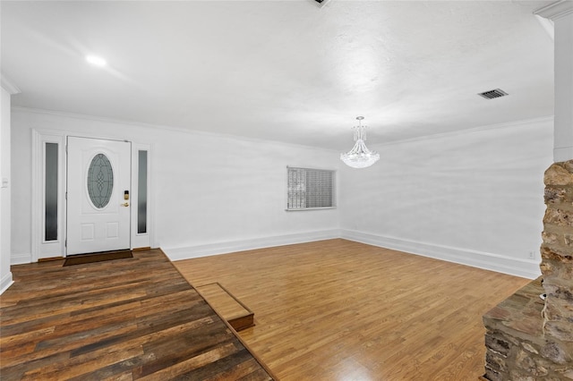 entryway with crown molding, dark wood-type flooring, and an inviting chandelier