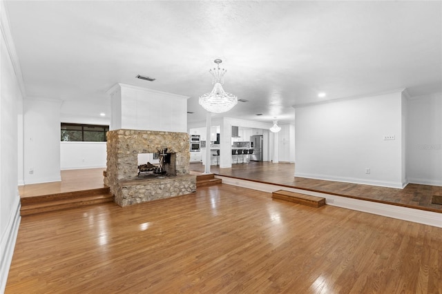 unfurnished living room featuring a notable chandelier, a stone fireplace, ornamental molding, and light wood-type flooring