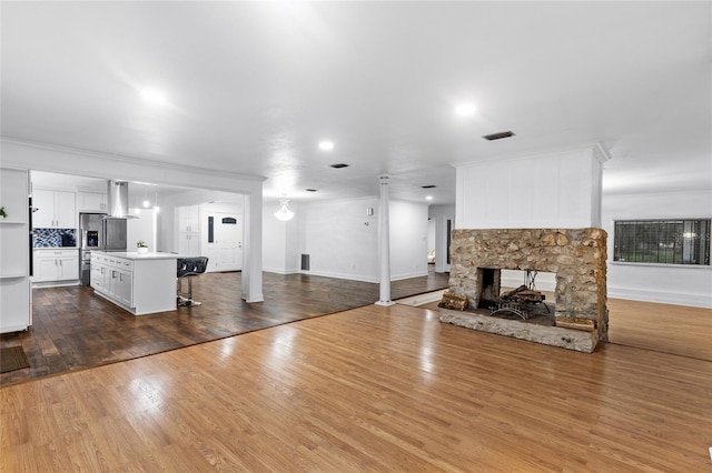 unfurnished living room with crown molding, a stone fireplace, and hardwood / wood-style floors