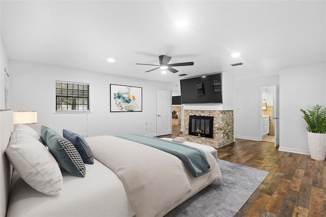 bedroom featuring ceiling fan, dark wood-type flooring, ensuite bathroom, and a fireplace