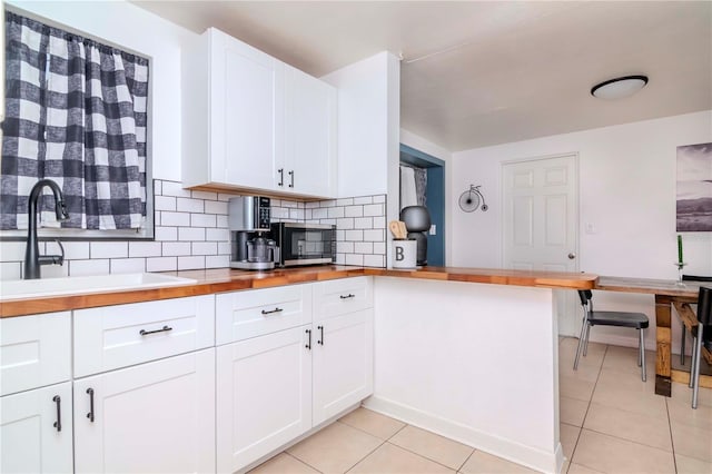 kitchen featuring kitchen peninsula, backsplash, white cabinets, light tile patterned flooring, and sink