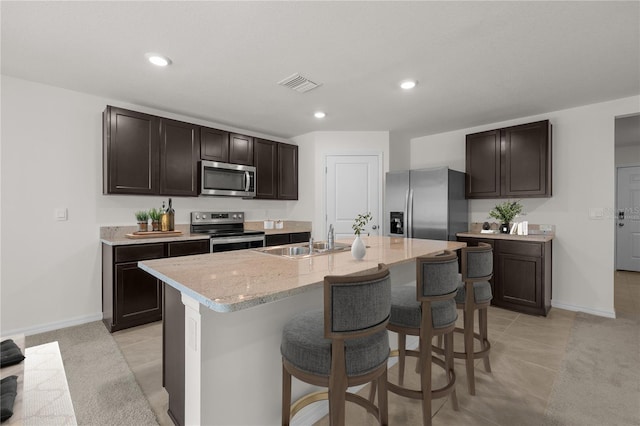 kitchen featuring a center island with sink, sink, appliances with stainless steel finishes, light tile patterned floors, and dark brown cabinets