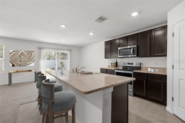 kitchen featuring sink, appliances with stainless steel finishes, an island with sink, light carpet, and dark brown cabinets