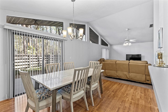 dining space with ceiling fan with notable chandelier, hardwood / wood-style flooring, and vaulted ceiling