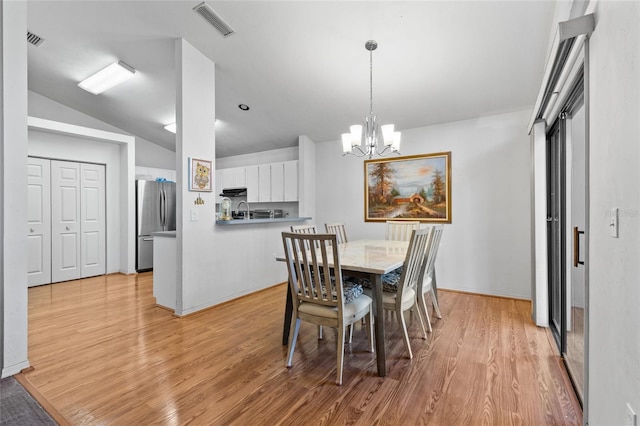 dining room with an inviting chandelier, vaulted ceiling, and light hardwood / wood-style flooring