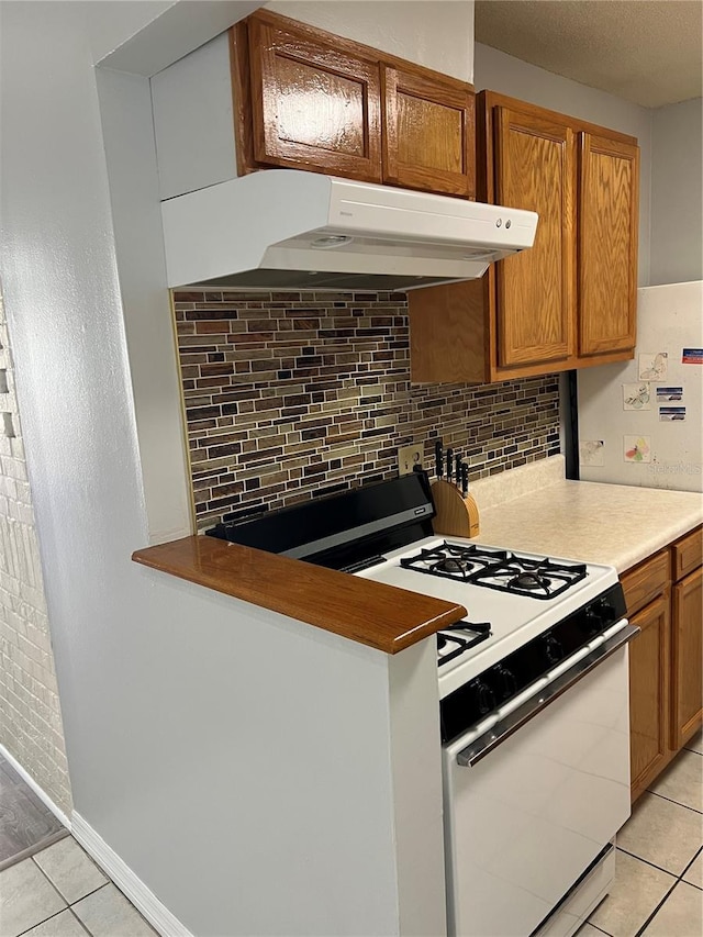 kitchen with white gas stove, decorative backsplash, and light tile patterned floors