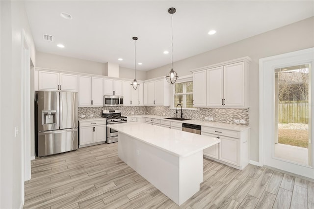 kitchen featuring sink, decorative light fixtures, appliances with stainless steel finishes, a kitchen island, and white cabinets