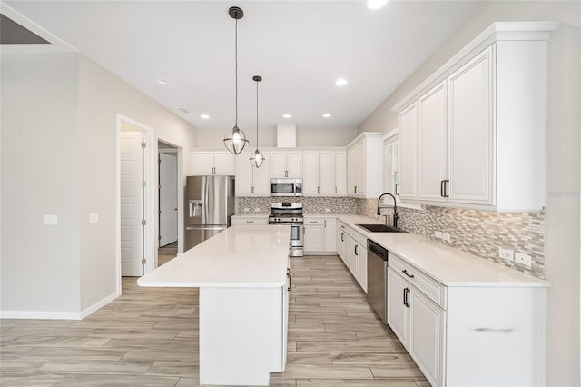 kitchen with sink, appliances with stainless steel finishes, a kitchen island, pendant lighting, and white cabinets