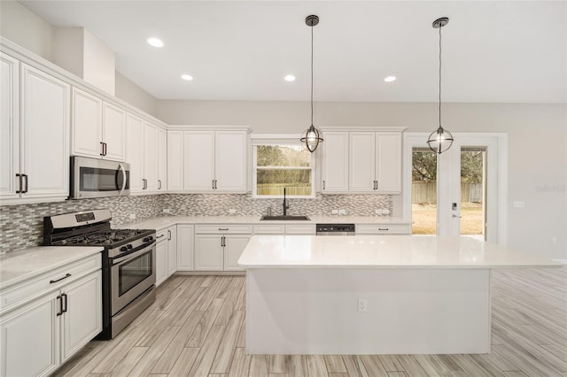 kitchen featuring pendant lighting, sink, appliances with stainless steel finishes, white cabinets, and a kitchen island