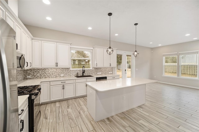 kitchen featuring sink, white cabinetry, decorative light fixtures, appliances with stainless steel finishes, and a kitchen island