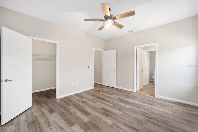 unfurnished bedroom featuring a walk in closet, ensuite bath, light hardwood / wood-style flooring, a closet, and ceiling fan