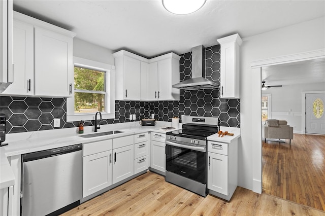 kitchen with stainless steel appliances, a sink, white cabinets, wall chimney exhaust hood, and light wood finished floors