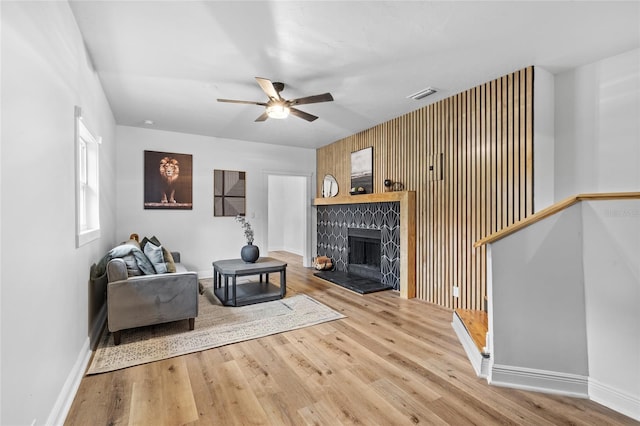 living area with ceiling fan, wood finished floors, visible vents, baseboards, and a tiled fireplace