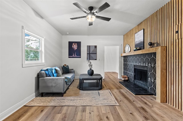 living area featuring a ceiling fan, a tiled fireplace, baseboards, and wood finished floors