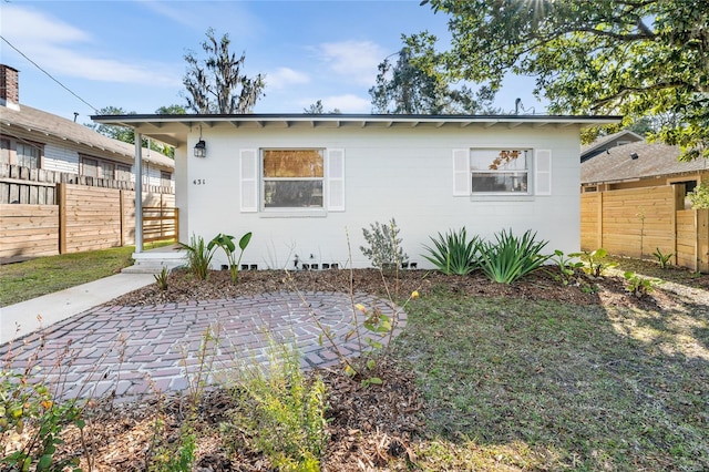 view of front facade with a patio, concrete block siding, and fence