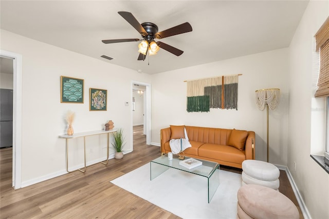 living room featuring a ceiling fan, visible vents, baseboards, and wood finished floors