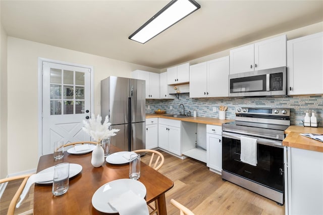 kitchen with stainless steel appliances, wooden counters, backsplash, light wood-style flooring, and white cabinetry