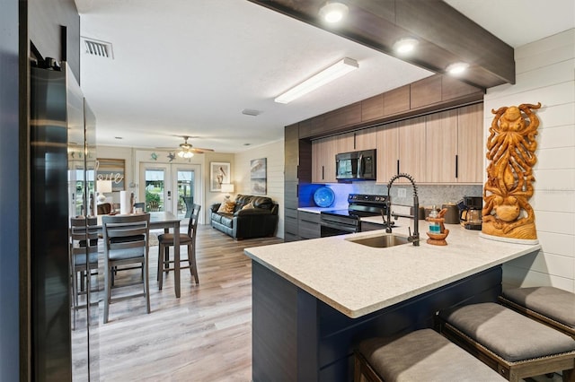 kitchen with kitchen peninsula, a kitchen bar, sink, light hardwood / wood-style flooring, and stainless steel range with electric cooktop