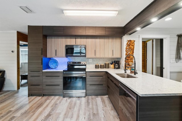 kitchen featuring appliances with stainless steel finishes, tasteful backsplash, sink, kitchen peninsula, and light hardwood / wood-style flooring