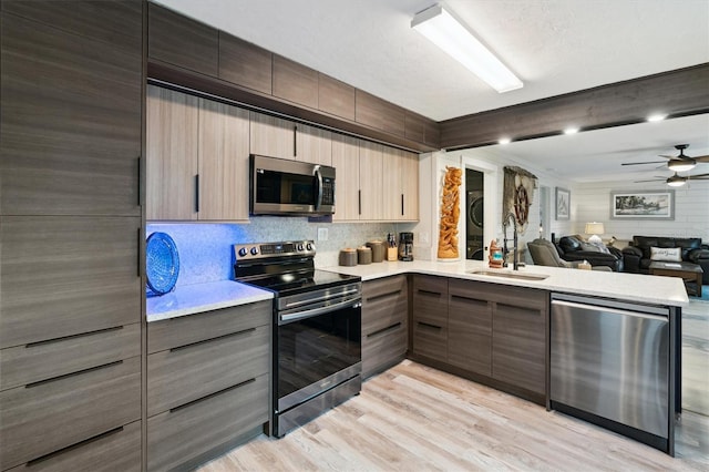 kitchen featuring ceiling fan, light hardwood / wood-style floors, sink, stacked washer and clothes dryer, and stainless steel appliances