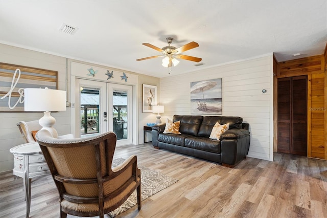 living room with ceiling fan, light hardwood / wood-style flooring, french doors, and wooden walls