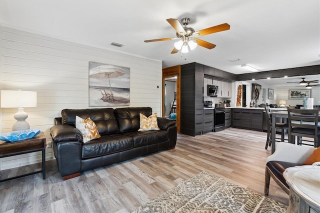 living room with ceiling fan, wood walls, and light hardwood / wood-style flooring