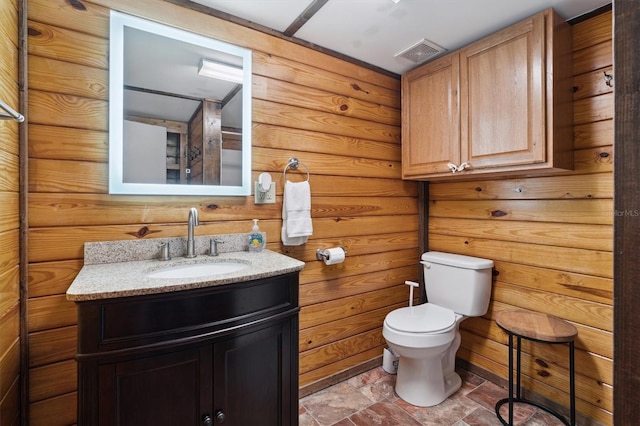 bathroom featuring toilet, wood walls, and vanity