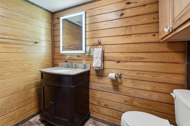 bathroom featuring toilet, vanity, and wood walls