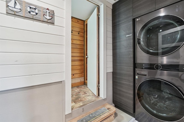 laundry area featuring stacked washer and clothes dryer and wooden walls