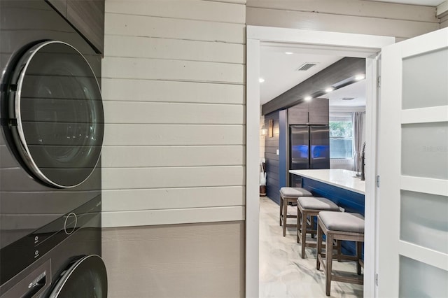 laundry area with stacked washer / drying machine and wood walls