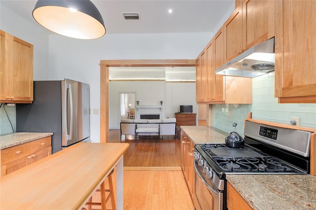 kitchen with stainless steel appliances, decorative backsplash, light hardwood / wood-style floors, and light stone countertops