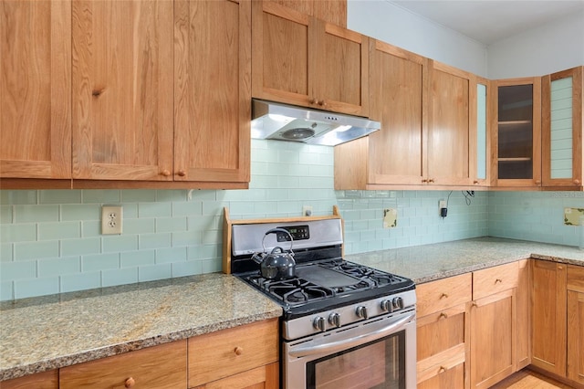 kitchen featuring light stone counters, backsplash, and stainless steel gas range oven