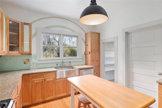 kitchen with decorative light fixtures, tasteful backsplash, stainless steel dishwasher, sink, and light stone countertops