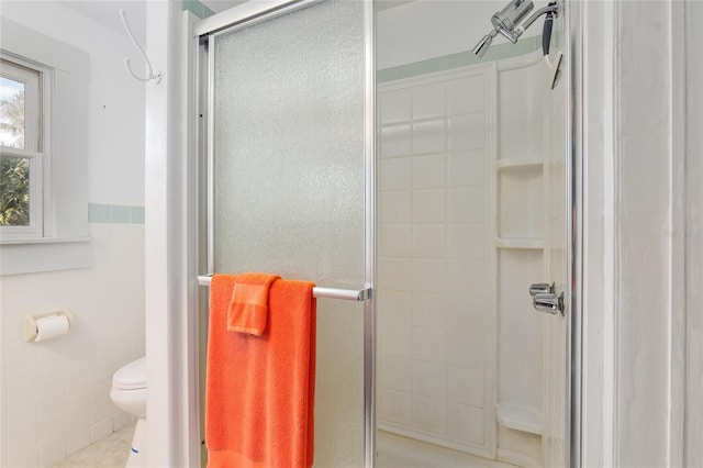 bathroom featuring a shower with shower door, tile walls, and toilet