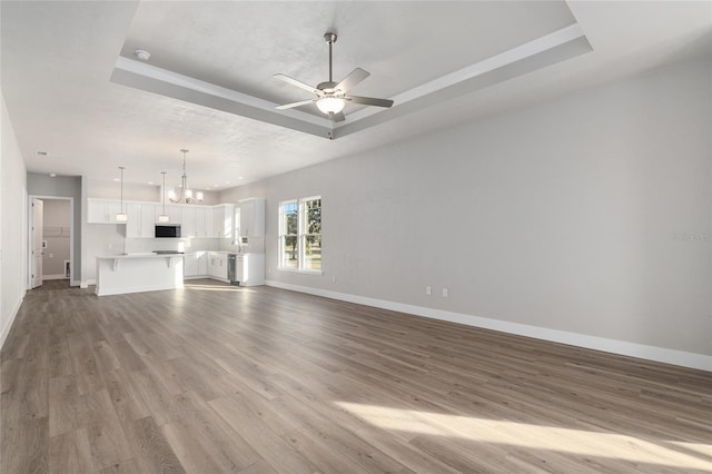 unfurnished living room with ceiling fan with notable chandelier, light hardwood / wood-style flooring, and a tray ceiling