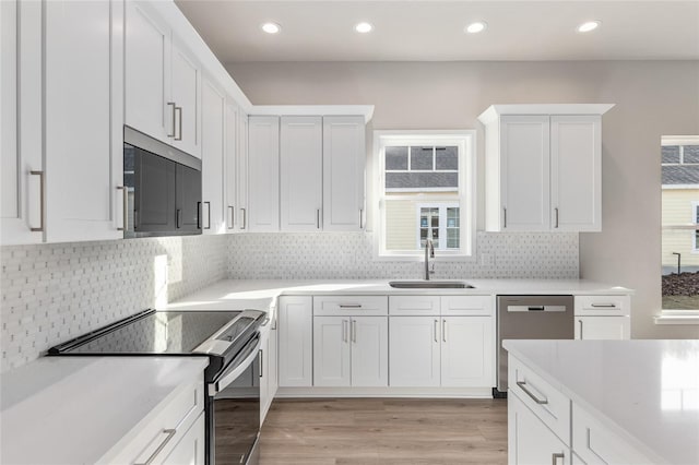 kitchen featuring light hardwood / wood-style floors, appliances with stainless steel finishes, backsplash, white cabinets, and sink