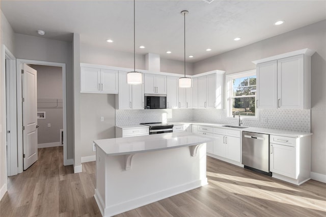 kitchen featuring white cabinetry, appliances with stainless steel finishes, hanging light fixtures, a kitchen island, and sink