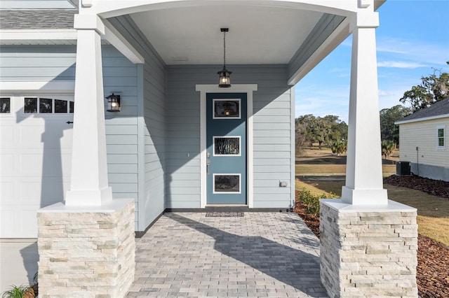 property entrance with covered porch, a garage, and central air condition unit