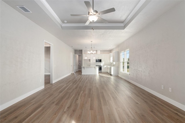 unfurnished living room featuring a raised ceiling, ceiling fan with notable chandelier, and hardwood / wood-style floors