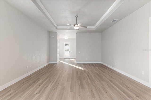 empty room featuring light wood-type flooring, ceiling fan, and a tray ceiling