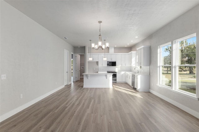 kitchen featuring white cabinets, a center island, decorative light fixtures, stainless steel appliances, and light wood-type flooring