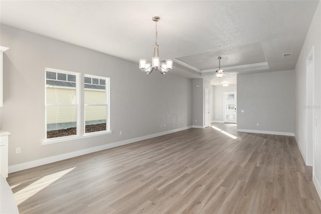 empty room with ceiling fan with notable chandelier, light hardwood / wood-style floors, and a raised ceiling